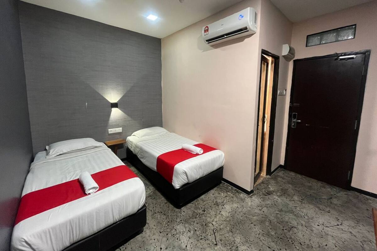 A hotel room with two beds, a wall-mounted air conditioner, a door, and a light fixture.