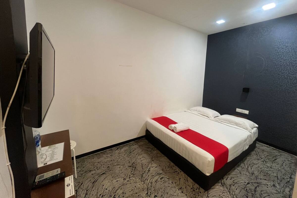A hotel room with a bed, a TV, and a desk with a computer and a water bottle.