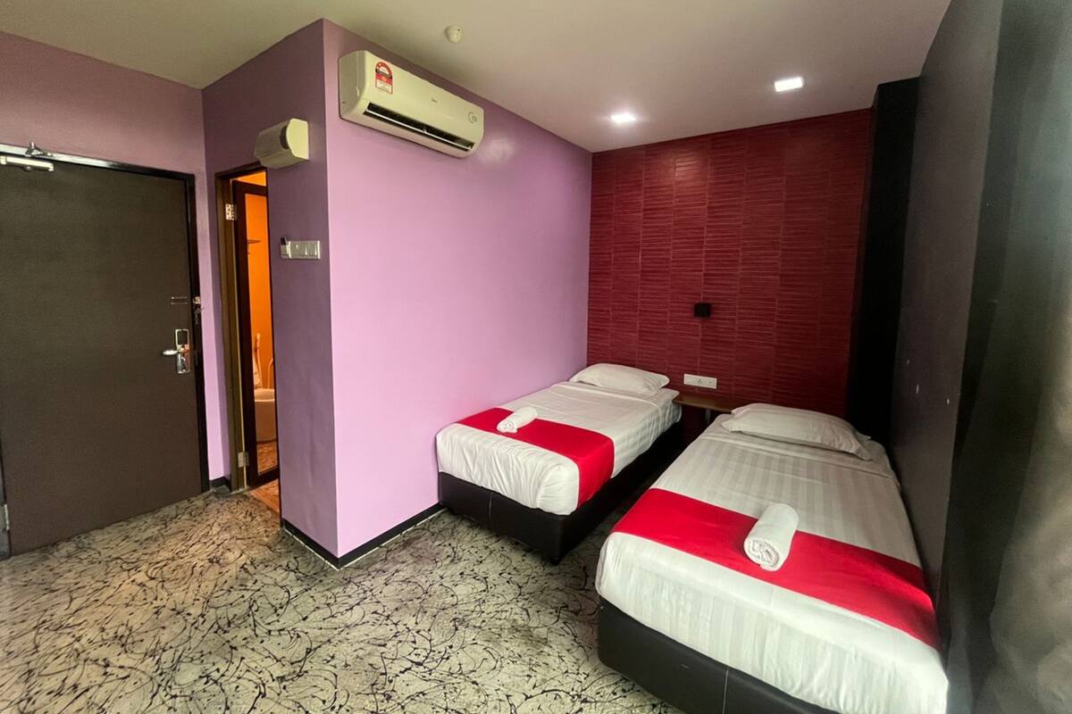 A hotel room with two beds, an air conditioning unit, a door, and a patterned floor.