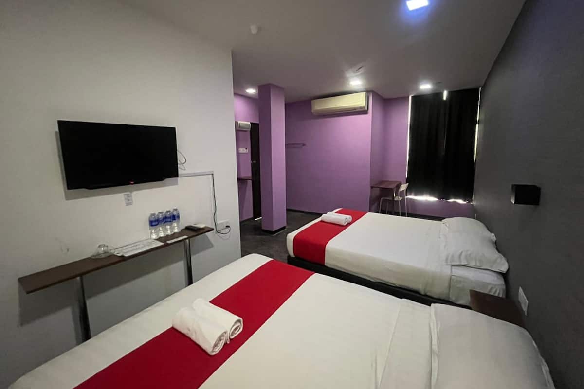 A hotel room with two beds, a TV, a desk with water bottles, and an air conditioning unit.