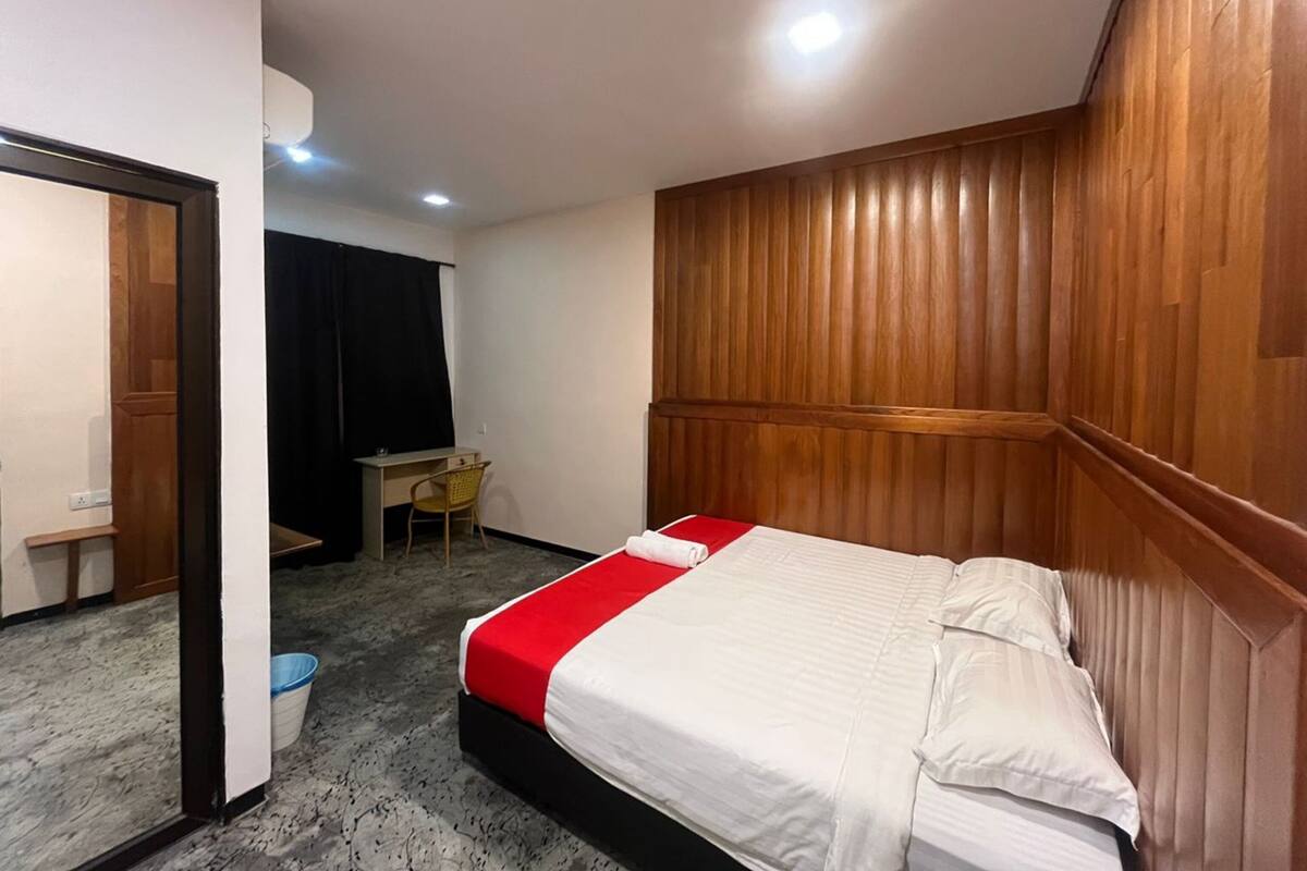 A hotel room with a bed, a desk, a chair, and a wooden headboard.