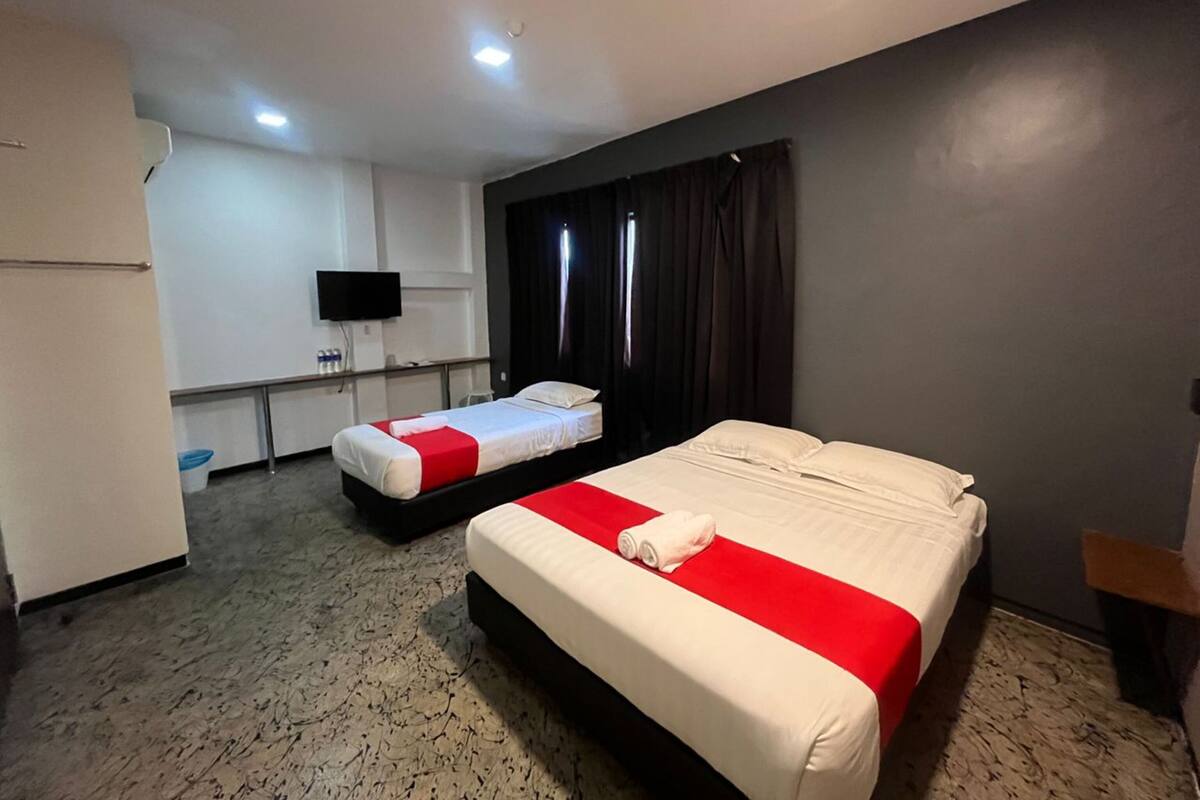 A hotel room with two beds, a flat-screen TV, a minibar, and a large window with curtains.
