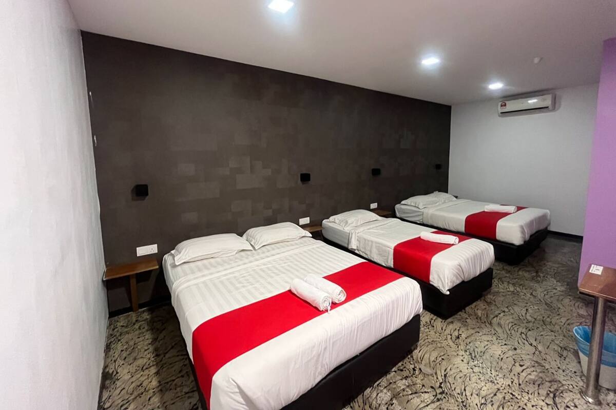 A hotel room with four beds arranged in a row, each with white bedding and red accents.