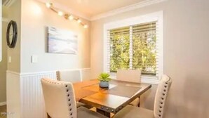 A dining area with a wooden table and four chairs, a small plant on the table, and a window with blinds.