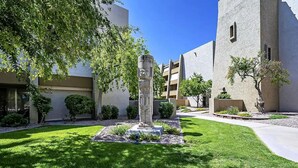 A courtyard with a central monument, surrounded by well-maintained grass and trees, and adjacent buildings with balconies.