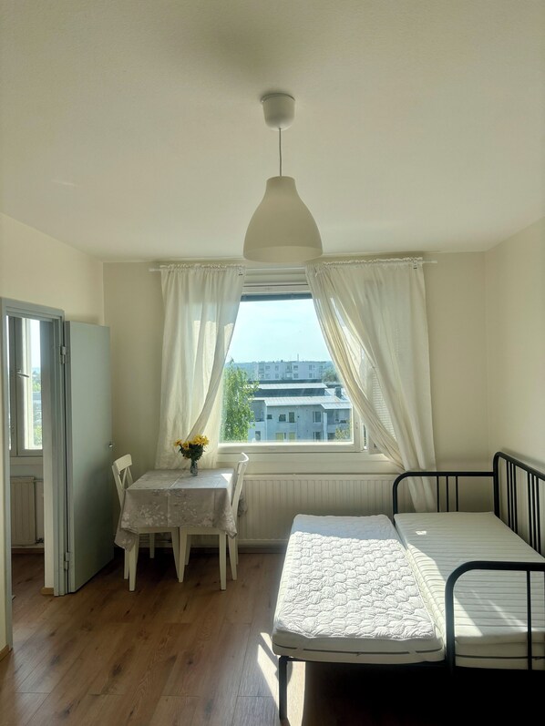 A bedroom with a bed, a table with a vase of flowers, a window with curtains, and a radiator.