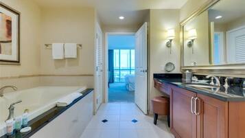 A modern bathroom with a large bathtub, a vanity with a mirror, and a view of a balcony through an open door.