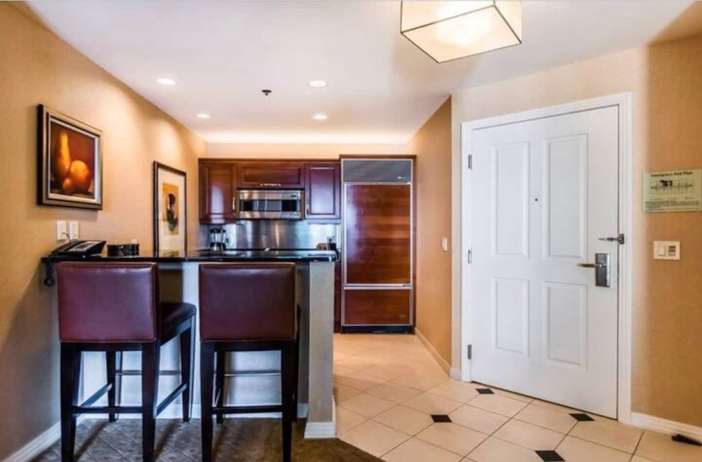 A compact kitchen with dark wood cabinets, stainless steel appliances, and a small island with two bar stools.