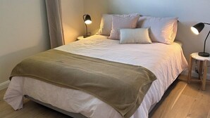 A bedroom with a large bed, two bedside lamps, a window with curtains, and a wooden floor.