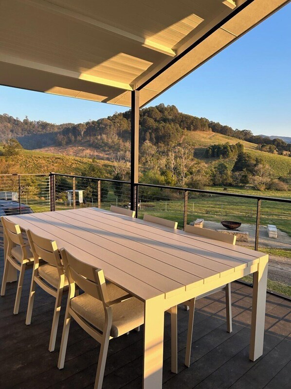 An outdoor patio with a wooden table and chairs, overlooking a hilly landscape. - Family-sized getaway in the heart of the Williams valley, near Barrington tops (Salisbury)