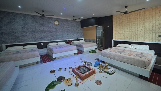 Une chambre d’hôtel avec trois lits, un mur en briques, des ventilateurs de plafond et un papier peint à motifs sur un des murs.