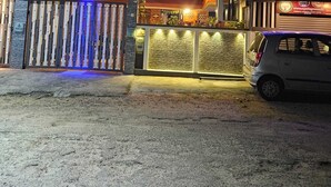 Un immeuble de deux étages doté d’un balcon, d’une entrée fermée par un portail et d’une voiture garée devant.