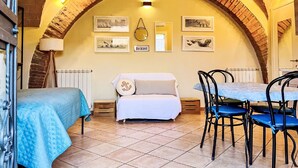 Una habitación acogedora con techo abovedado de ladrillo, cama, sofá, mesa con sillas y obras de arte en las paredes.