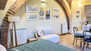 Una habitación acogedora con un arco de ladrillo, una cama, un escritorio y un radiador.