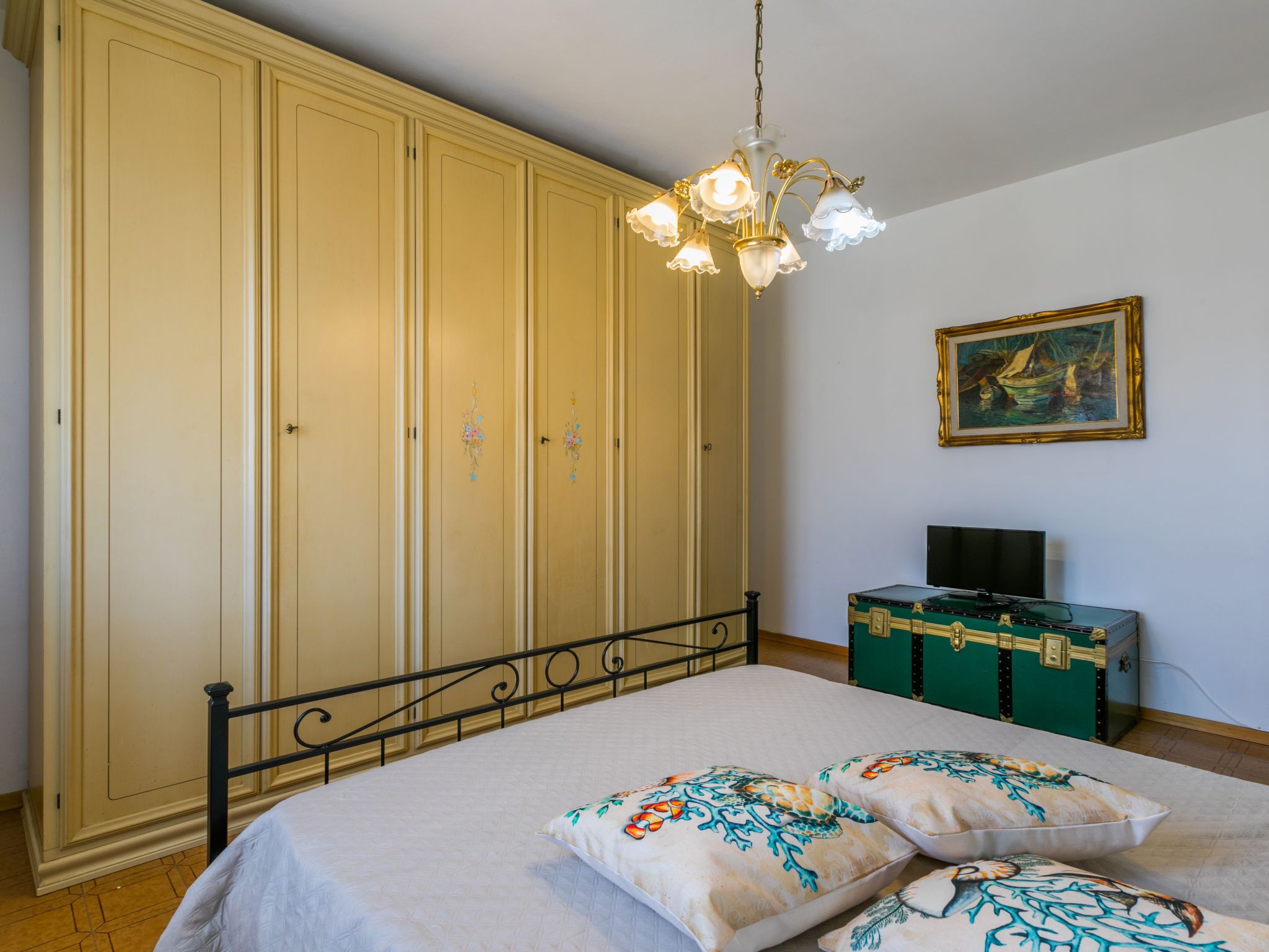 A bedroom with a bed, a wardrobe, a television, and a painting on the wall.