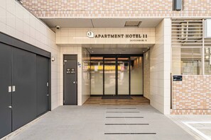 An entrance to an apartment hotel with a tiled facade, a sign above the entrance, and a set of double doors. - Apartment Hotel 11 Dotonbori II (Osaka)