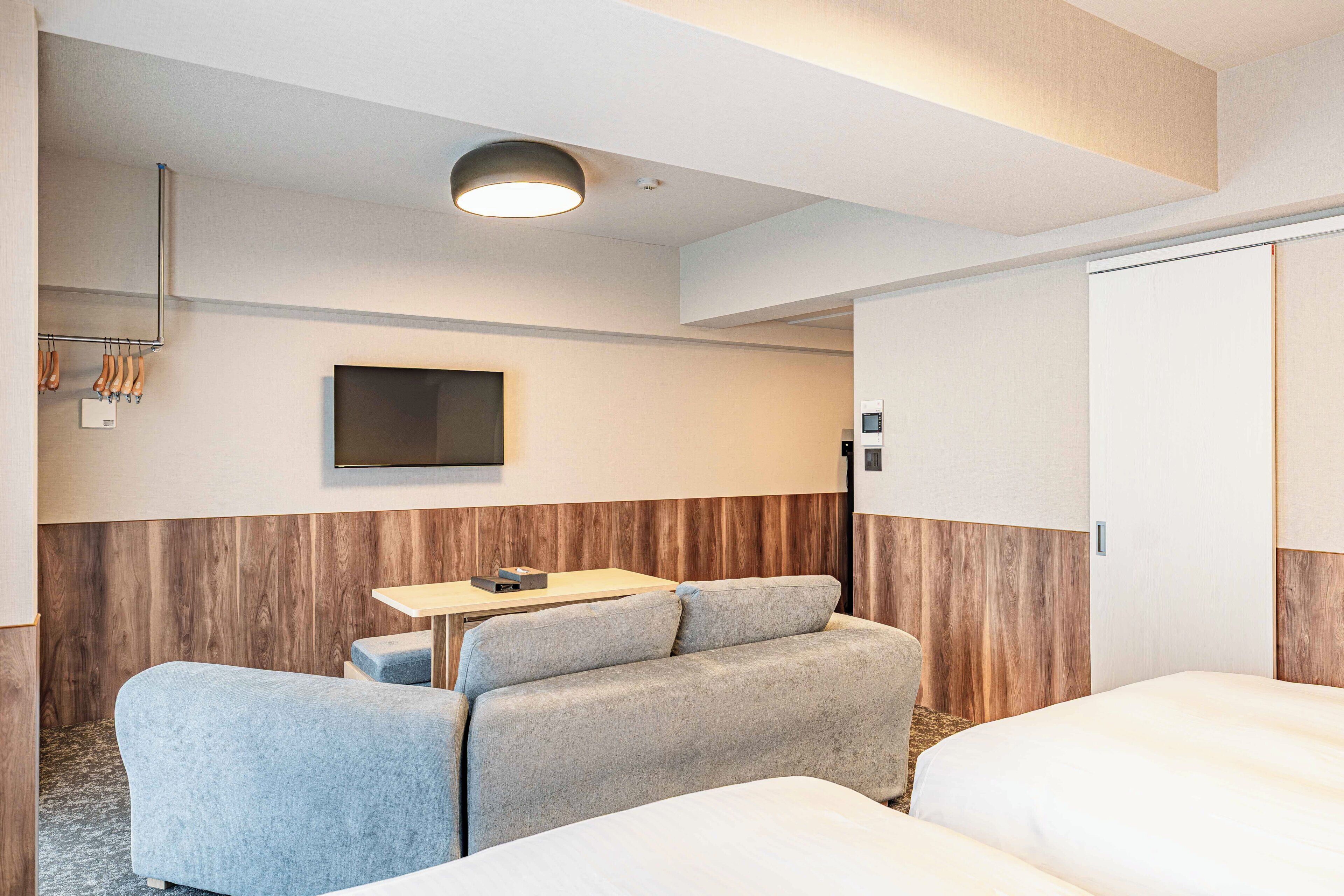 A hotel room with a sofa, a small table, a TV, and a wardrobe.