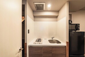A compact kitchen with a gas stove, sink, and a black refrigerator. - Apartment Hotel 11 Dotonbori II (Osaka)