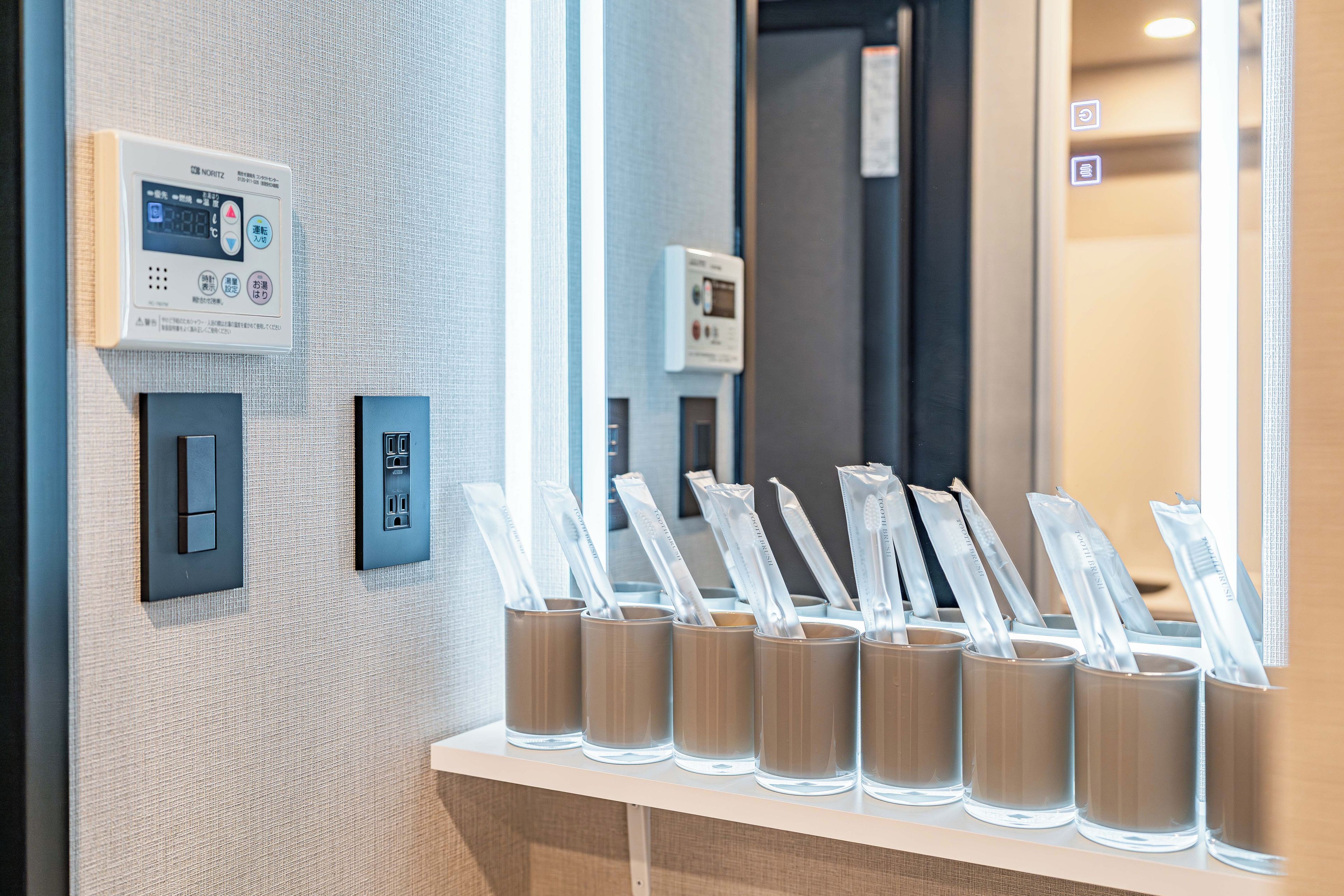 A hotel room with a thermostat, a power outlet, and a row of toothbrushes in holders.