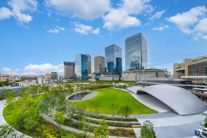 A modern urban landscape with high-rise buildings, a central green park, and a distinctive curved architectural feature. - Apartment Hotel 11 Dotonbori II (Osaka)