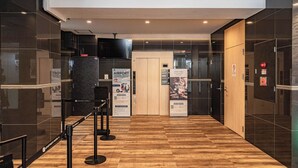 Egy modern szállodai előcsarnok, amelyben található egy recepció, fa padló és üvegfalak.