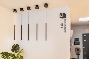 Moderni hotellin sisustus, jossa on pelkistetty muotoilu. Tilan tunnelmaa täydentää seinälle asennettu valaisin ja kyltti, jossa on hotellin nimi.