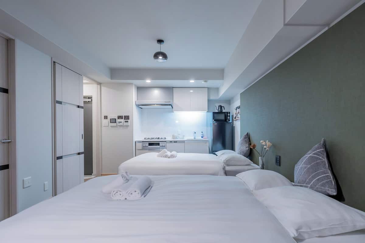 A hotel room with two beds, a kitchenette, and a bathroom.