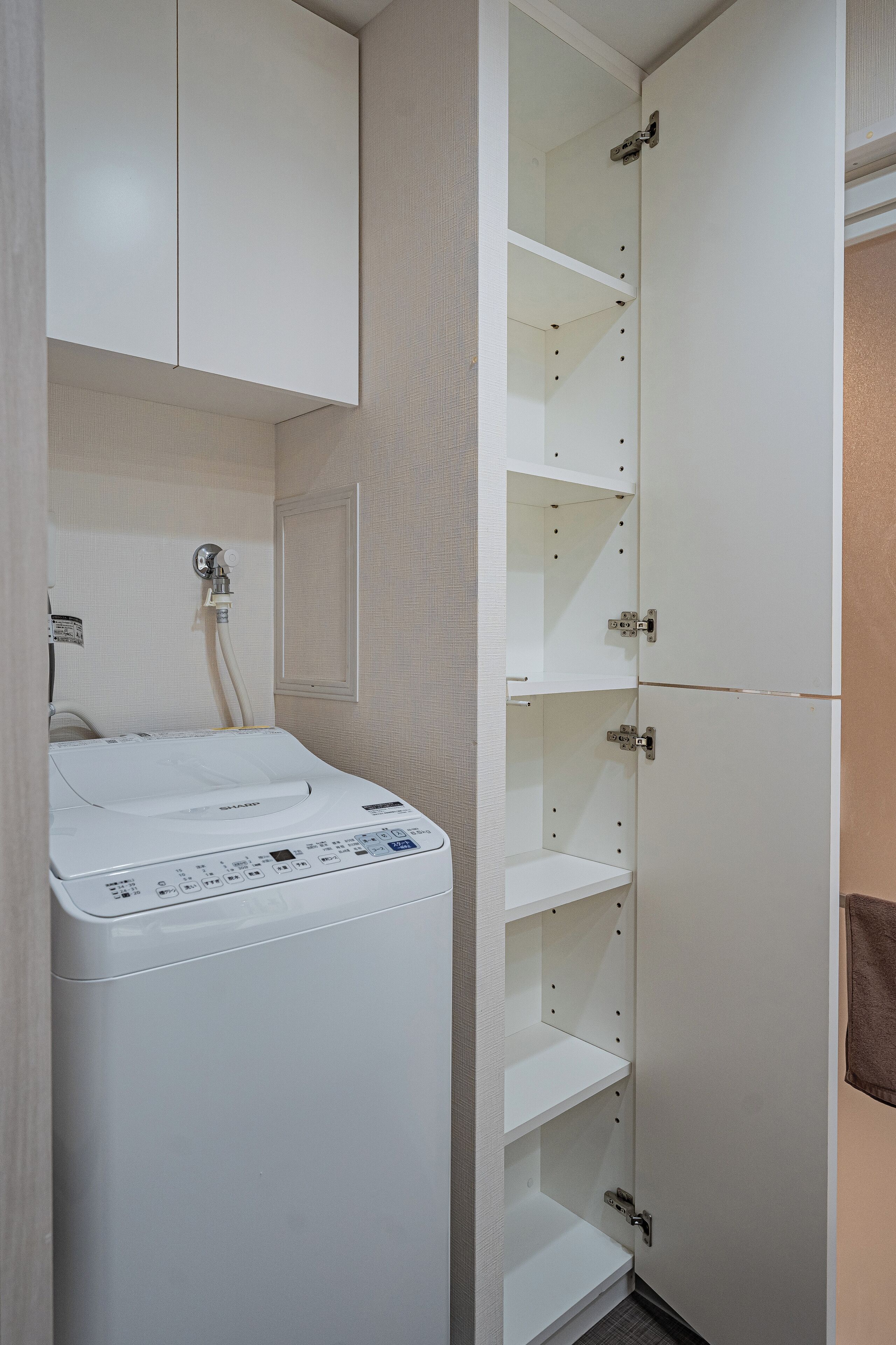 A compact laundry room with a washing machine, a drying rack, and a tall white cabinet with shelves.