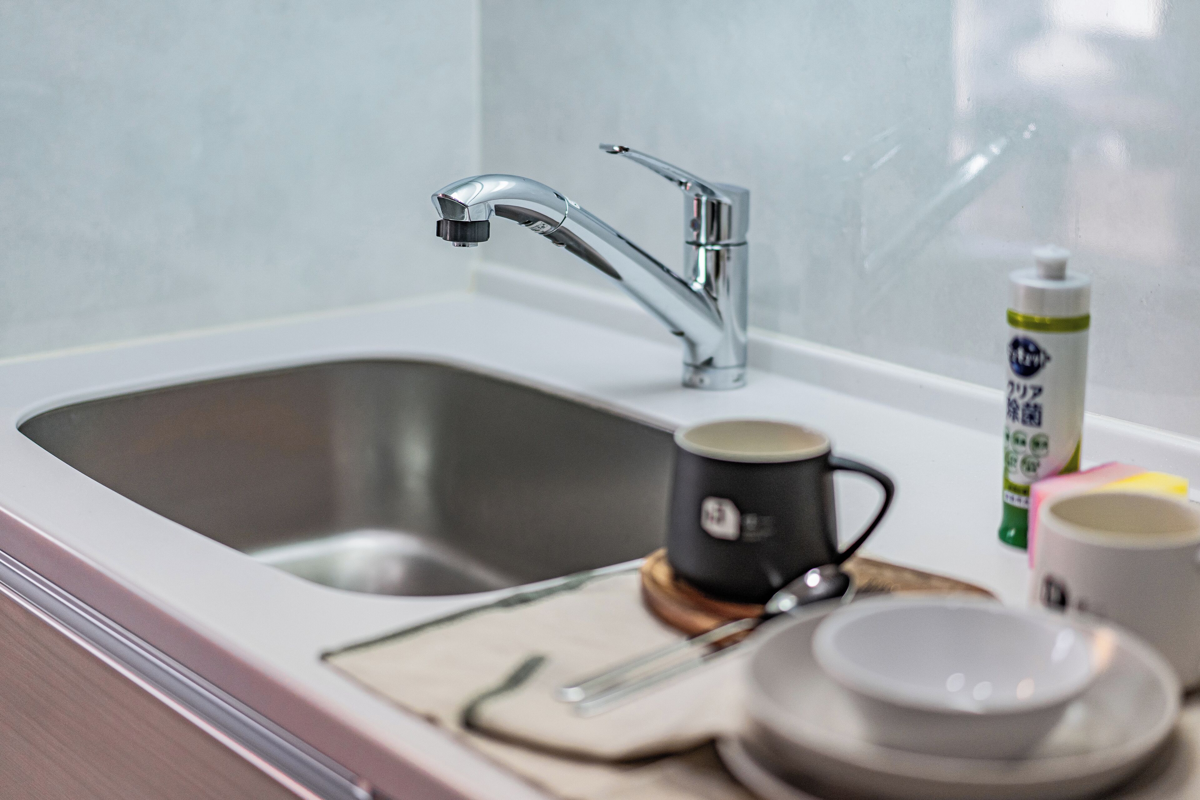 A modern kitchen sink with a chrome faucet, a coffee maker, and a bottle of dish soap on the counter.