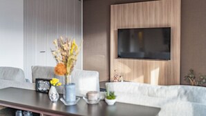 Ein modernes Wohnzimmer mit einem Wand-Fernseher, einer Couch, einem Couchtisch mit Dekoration und einem großen Fenster.
