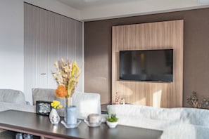 A modern living room with a flat-screen TV mounted on the wall, a sofa, a coffee table with decorative items, and a large window. - Apartment Hotel 11 Shinsaibashi (Osaka)