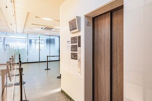 Ein moderner Aufzug mit digitaler Anzeige, einer Holztür und Hinweisschildern an der Wand.