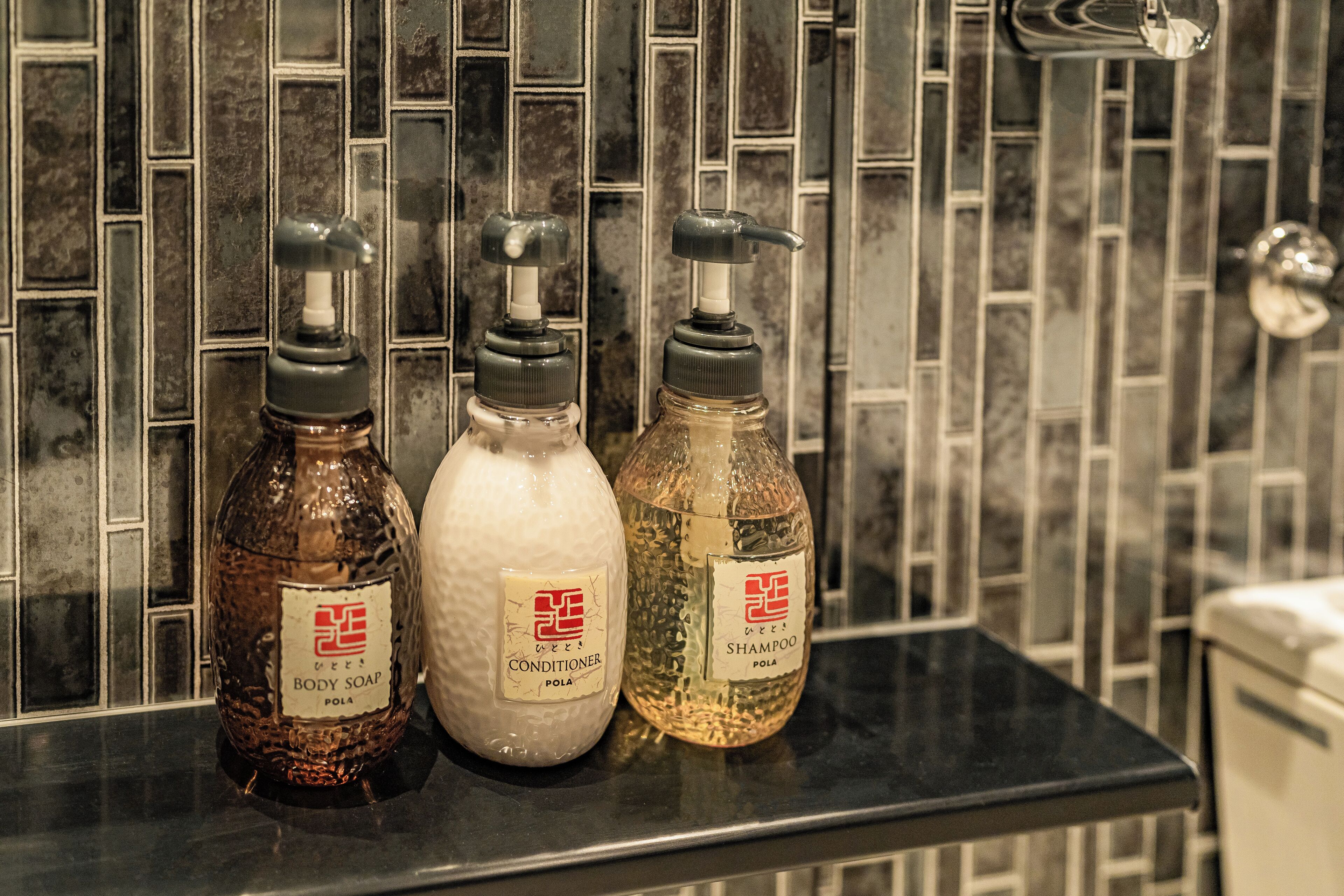 Three bottles of toiletries on a black countertop with a tiled backsplash.