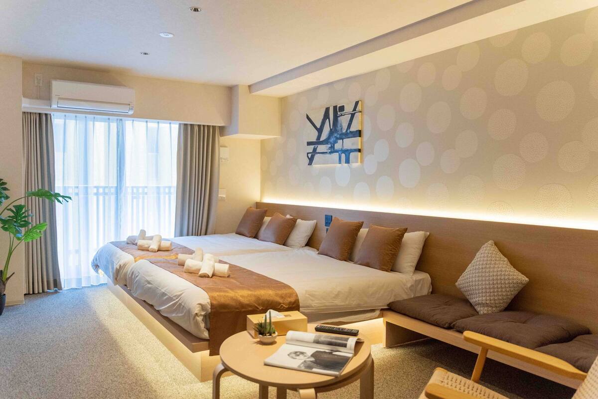 A hotel room with a large bed, a sofa, a small table, and a potted plant.