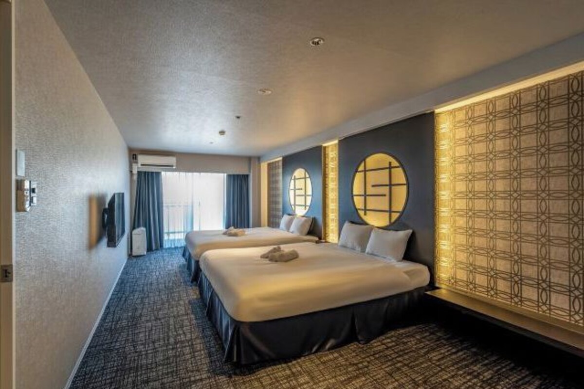 Ein Hotelzimmer mit zwei Betten, einem großen Fenster und einer dekorativen Wandverkleidung.