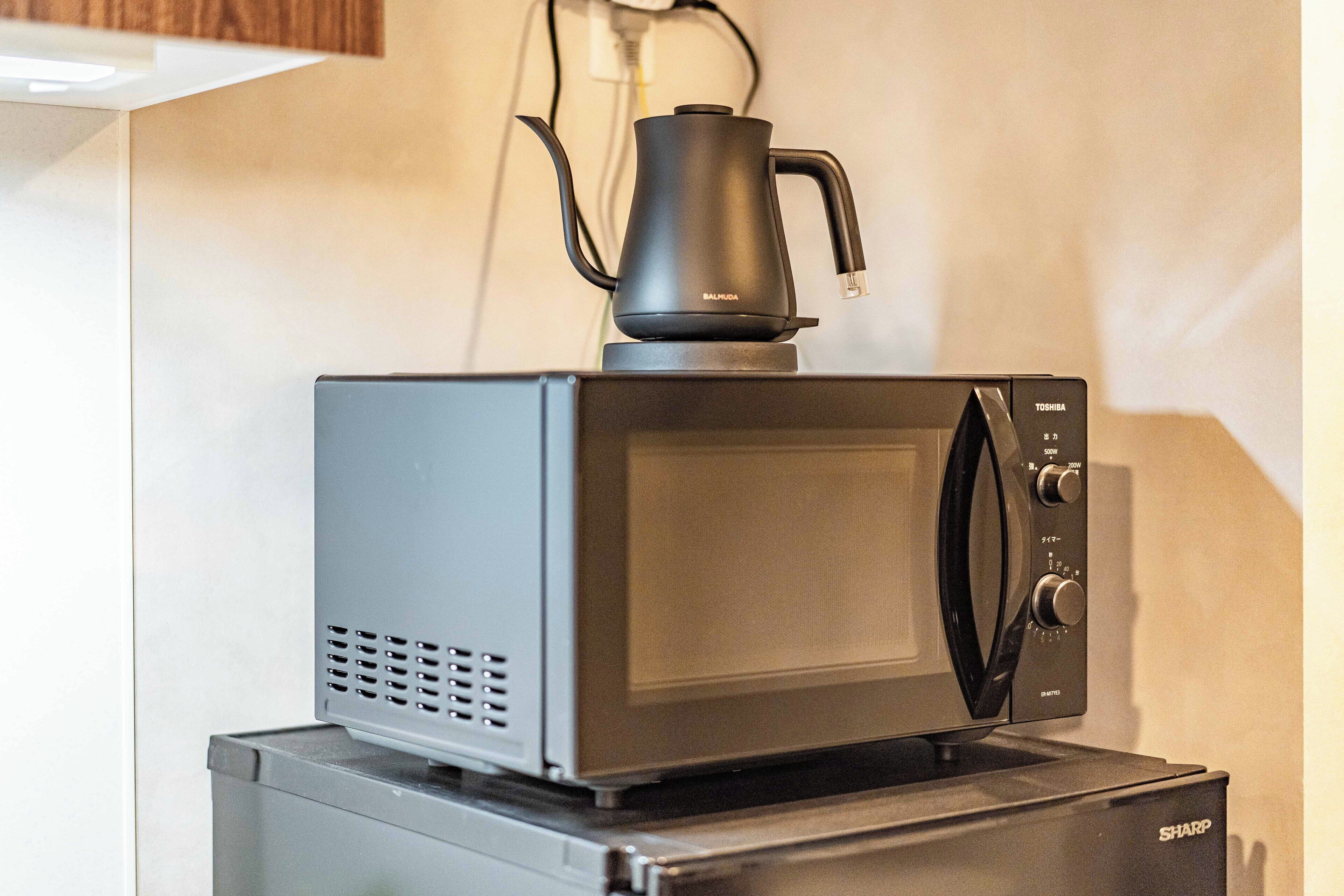Un four à micro-ondes avec une bouilloire posée sur le dessus, installé sur un réfrigérateur.