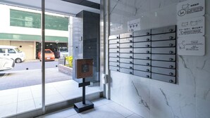 A hotel lobby with a glass door entrance, a marble wall with a mail slot, and a parking view outside. - Apartment Hotel 11 Kuromon II (Osaka)