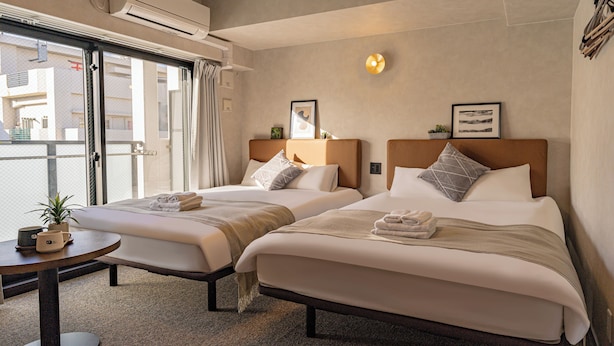 A hotel room with two beds, a small table with a plant, and a window with a view of buildings. - Apartment Hotel 11 Kuromon II (Osaka)