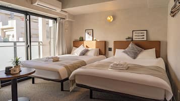 Quarto de hotel com duas camas, uma mesinha com uma planta e uma janela com vista para prédios.