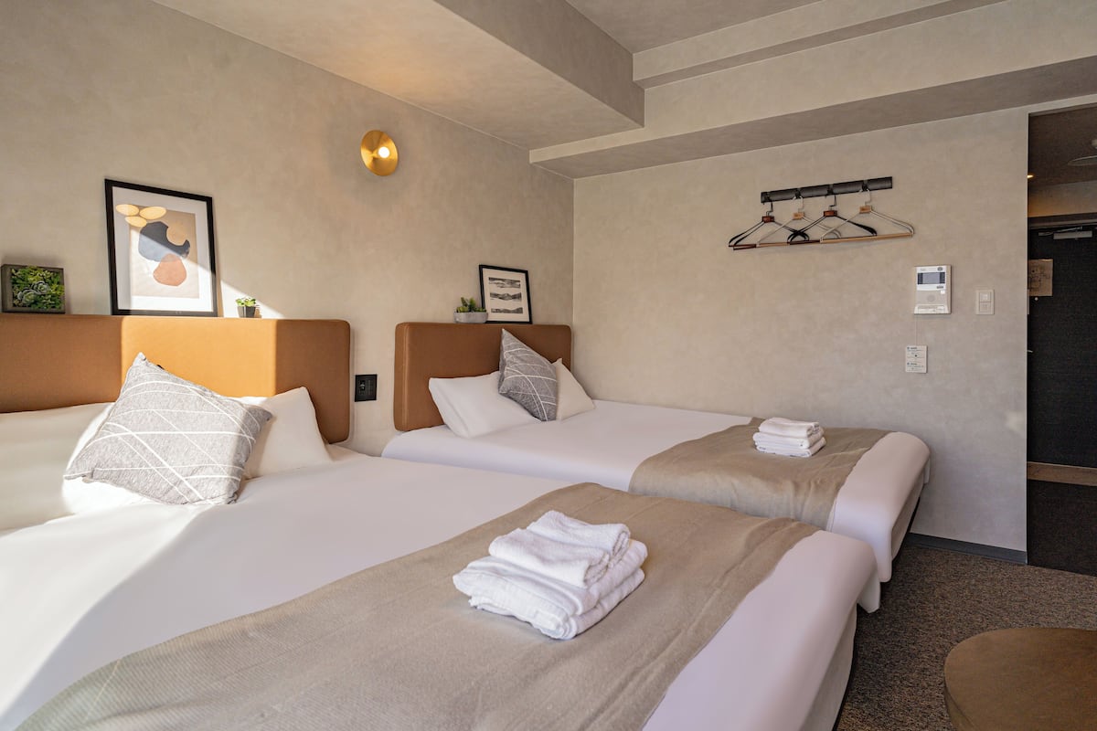 Une chambre d’hôtel avec deux lits, chacun doté d’une tête de lit, d’un luminaire fixé au mur et d’un tableau encadré au-dessus des lits.