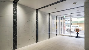 A lobby with marble walls and a tiled floor, leading to a glass door. - Apartment Hotel 11 Kuromon II (Osaka)