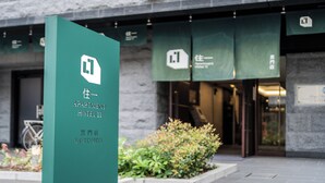 Señalización de 'Apartment Hotel 11' con un logotipo, fachada de edificio de piedra y toldo verde con el mismo logotipo.