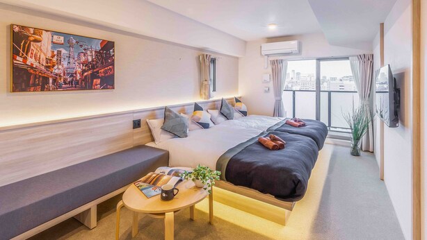 Una habitación de hotel moderna con una cama grande, un sofá, una mesita y un cuadro con una vista urbana.