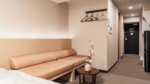 A hotel room with a sofa, a small table with a vase, a coat rack, and a refrigerator. - Apartment Hotel 11 Namba Minami III (Osaka)