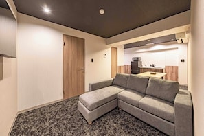 A modern living room with a grey sectional sofa, a wooden door, and a kitchen area in the background. - Apartment Hotel 11 Shinsaibashi 4 (Osaka)