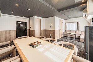 Una habitación de hotel moderna con zona de comedor, un conjunto de sofás y un refrigerador.
