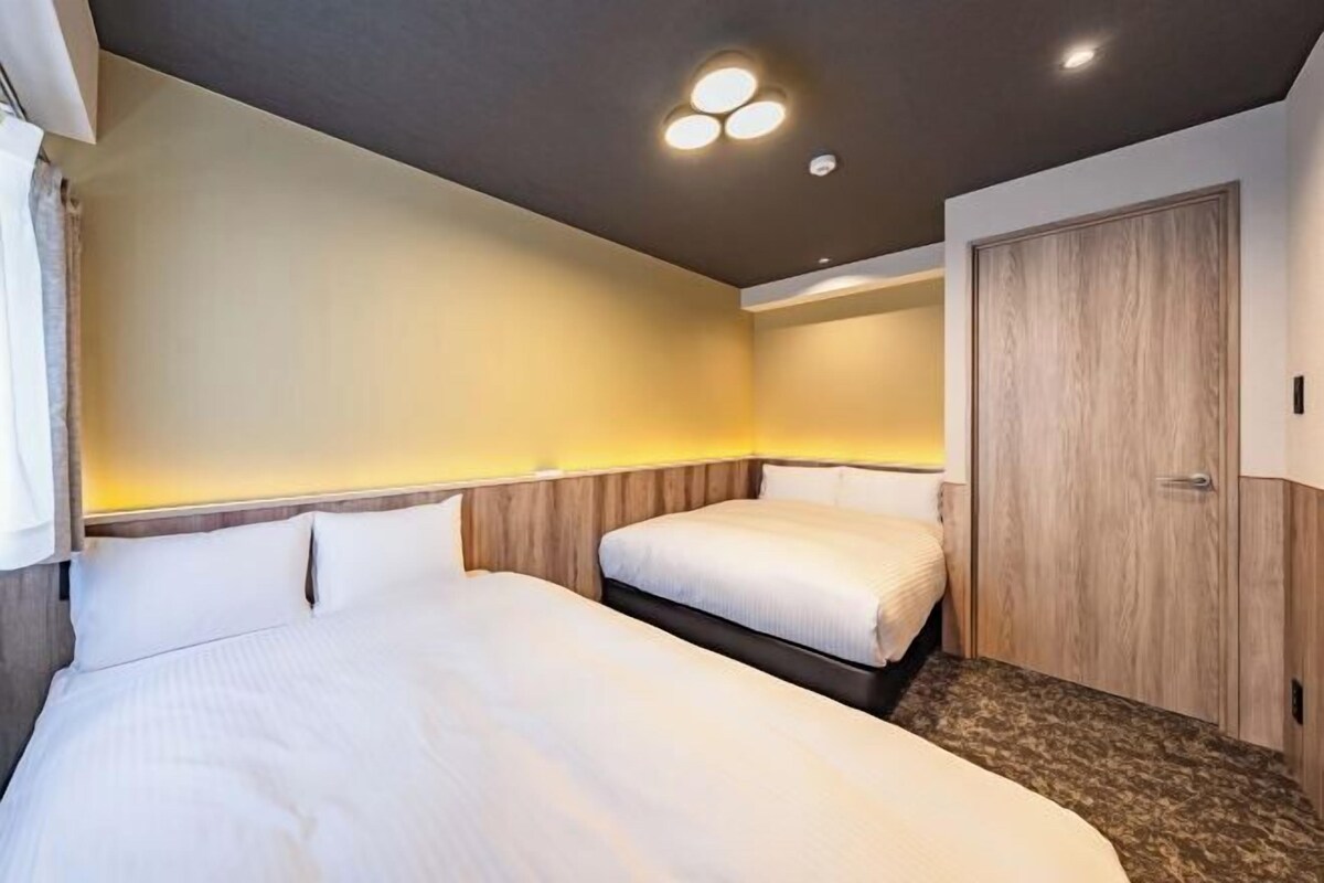 A hotel room with two beds, a wooden wardrobe, and a ceiling light fixture.