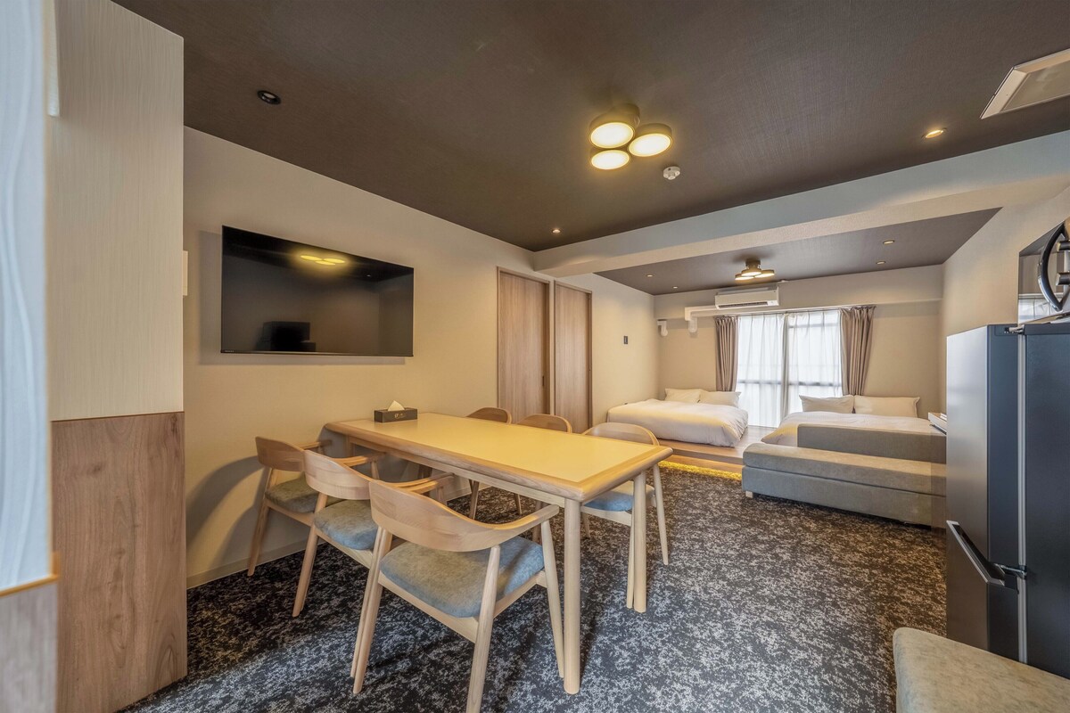 A compact hotel room with a dining area, a bed, a sofa, and a kitchenette.