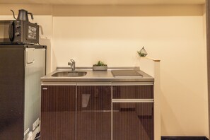 A compact kitchen with a refrigerator, microwave, sink, and a small potted plant.