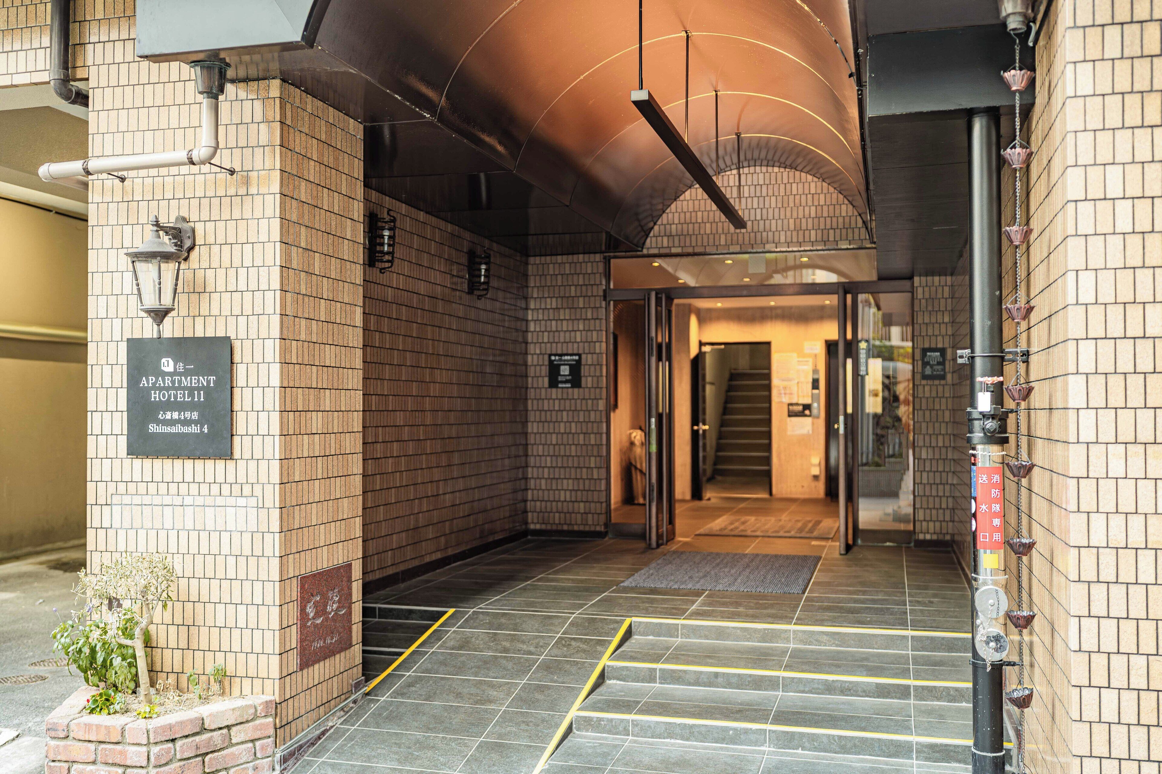 A hotel entrance with a brick facade, a sign indicating the name and location, and a staircase leading to the interior.